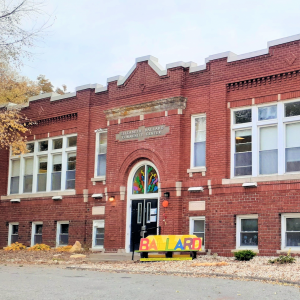 multi story red brick building with ballard center sign in front