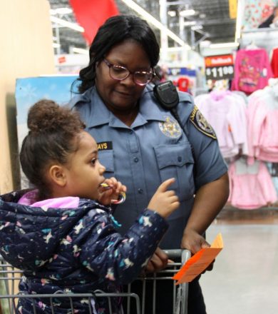 a female police officer in uniform next to a shopping cart with a child in in and pointing to something she wants