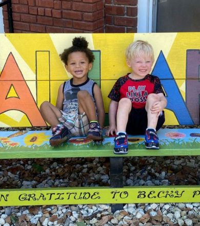 two young children sitting on a multi colored bench. both have their legs up and are smiling