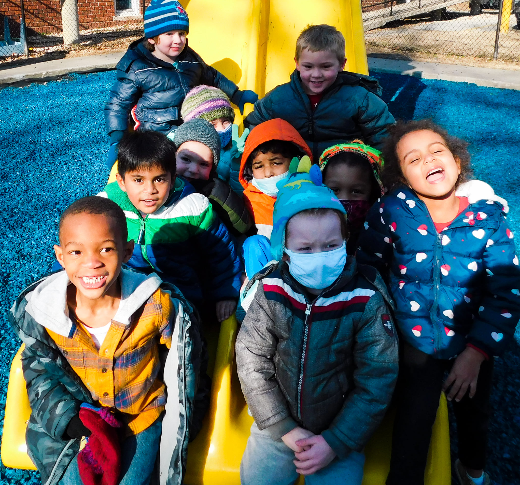 group of children dressed for the cold all sitting on a large yellow slide