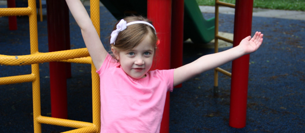 young girl wearing a pink t-shirt with her hands thrown up in the air