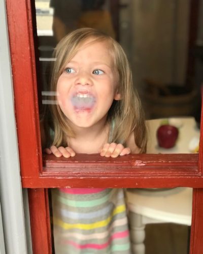 young girl blowing her breath onto a window and making it foggy
