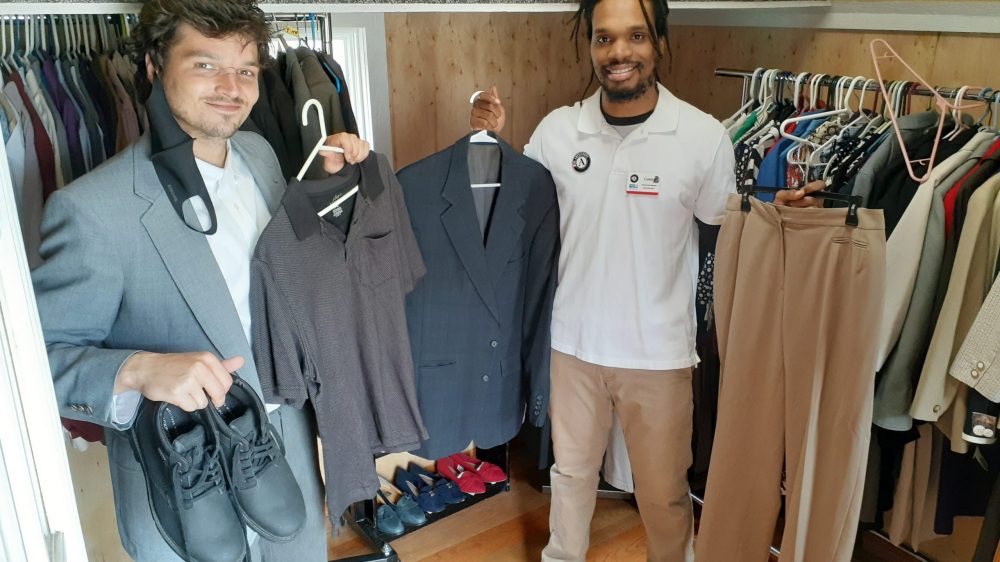 two men holding up shoes and shirts in front of racks of shoes and clothes